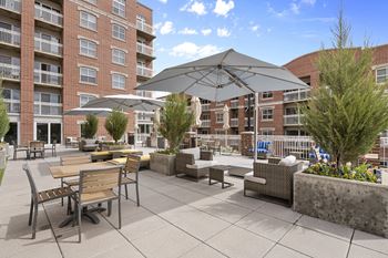 A patio with tables and chairs and umbrellas is surrounded by apartment buildings.